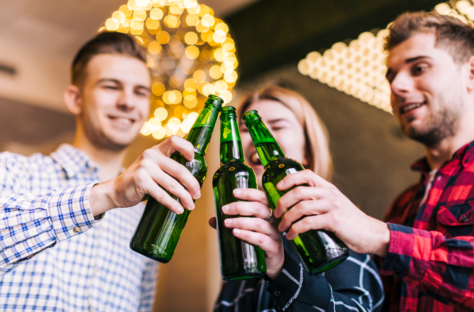 two men and a lady clinking/cheers their three green bottles of alcohol in a New Years setting
