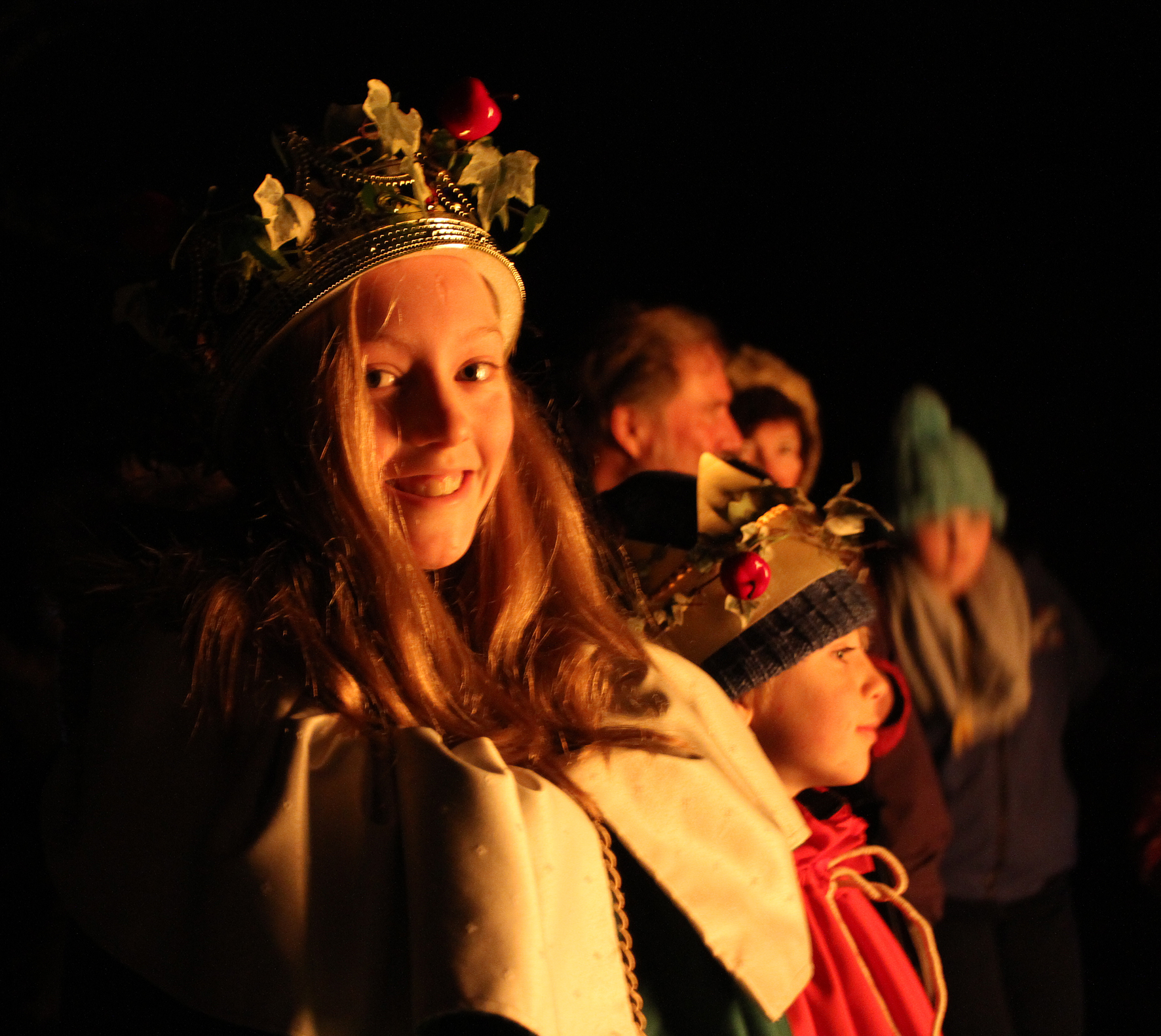 a young girl facing the camera smiling with a gold crown wrapped in ivy leaves - the Wassail crowned queen