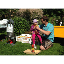Man and child holding apples next to a fruit press.