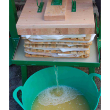 Apple juice pouring from pack press into green tub.